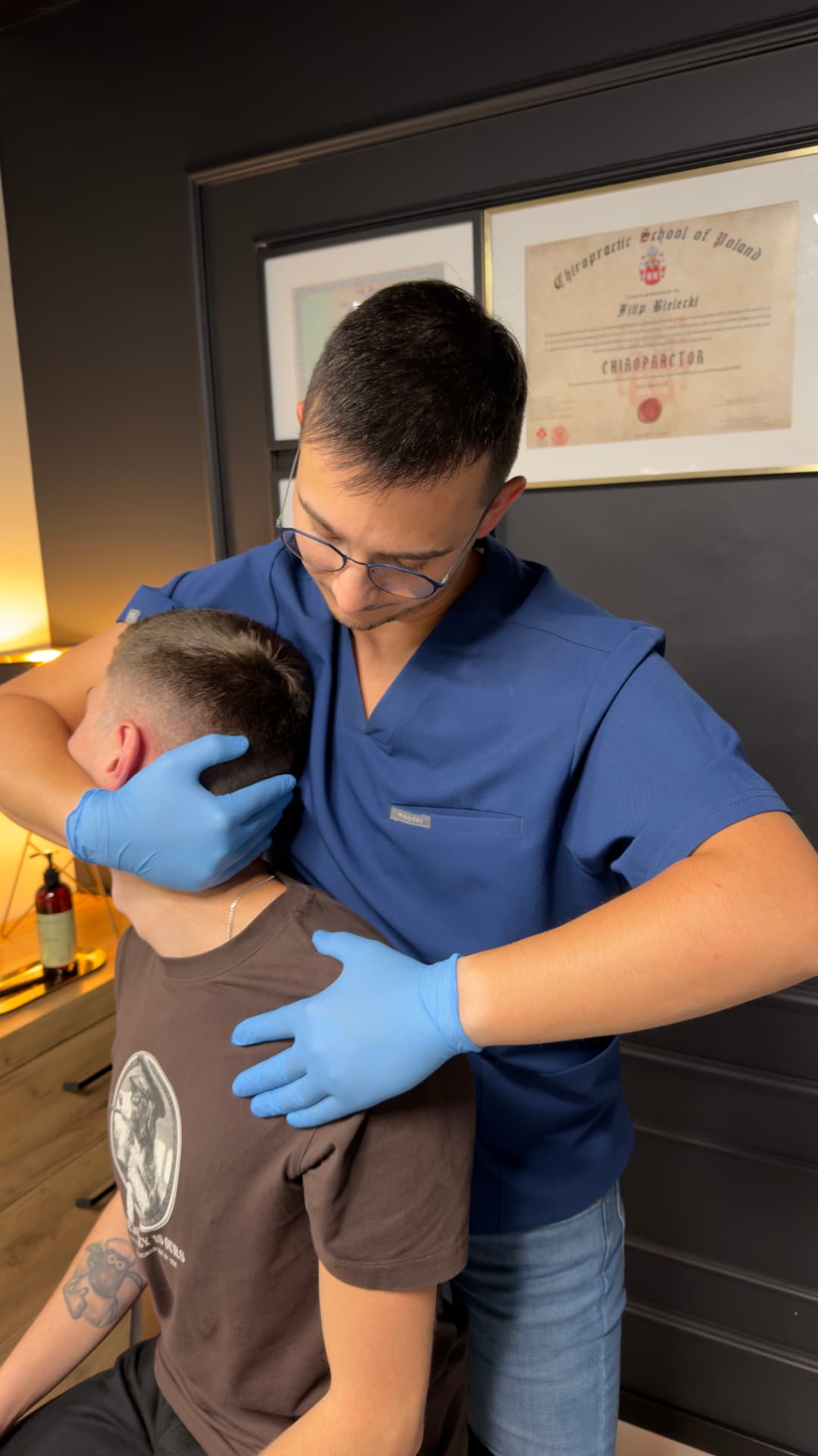 Filip Bielecki podczas terapii w gabinecie, w tle dyplom Chiropractic School of Poland